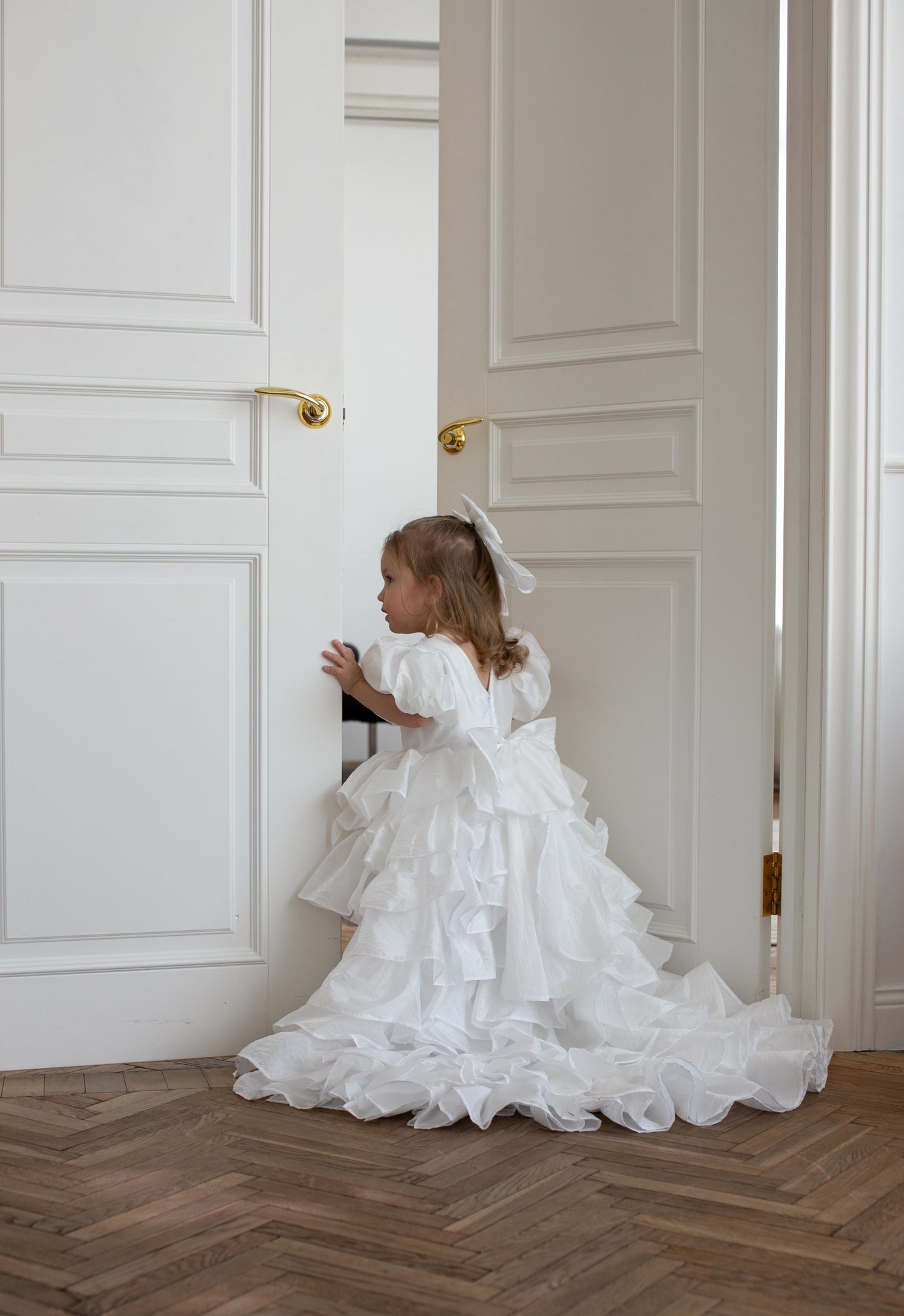 Petite fille vêtue d’une robe blanche volumineuse à volants et traîne