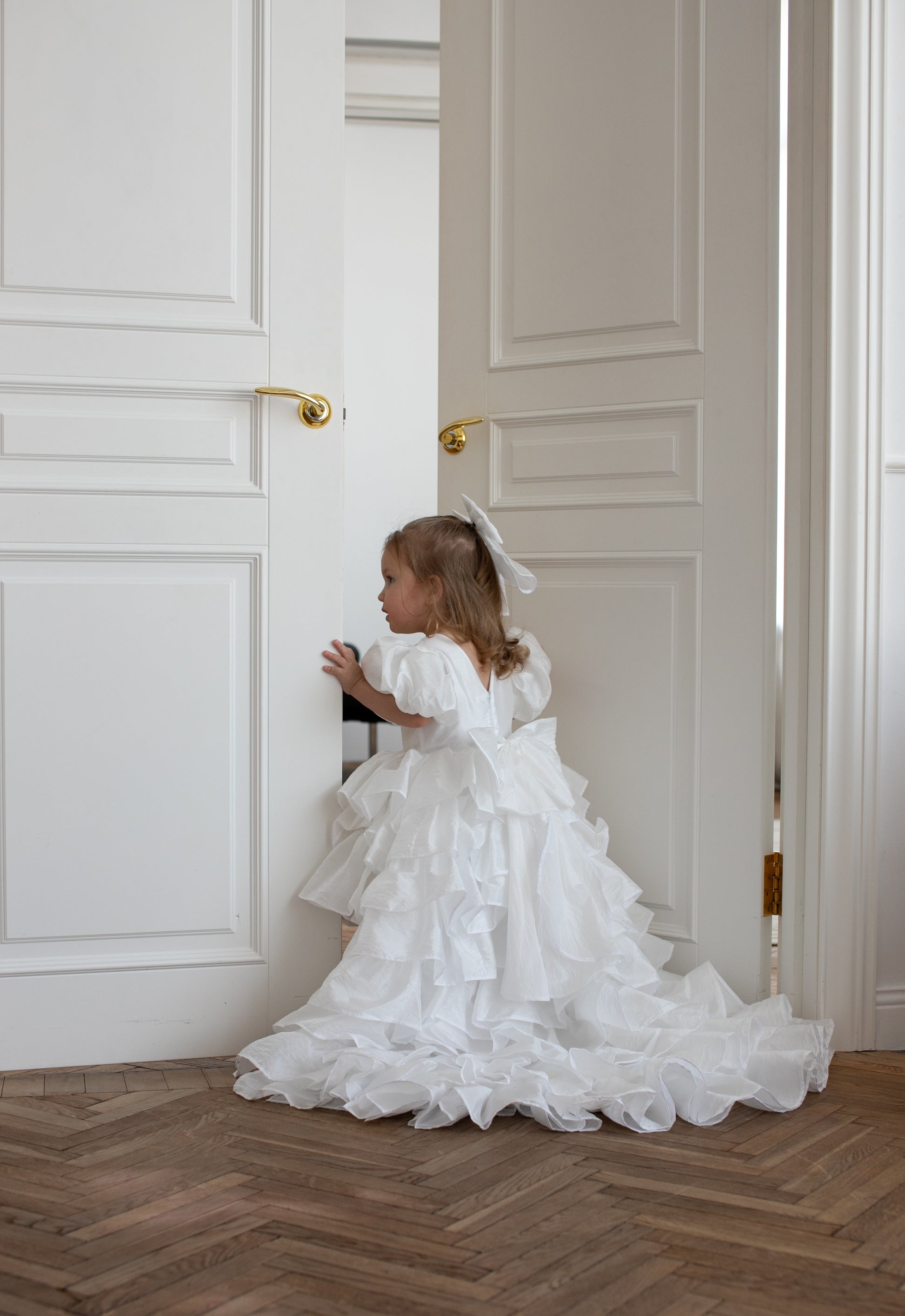 Petite fille vêtue d’une robe blanche volumineuse à volants et traîne