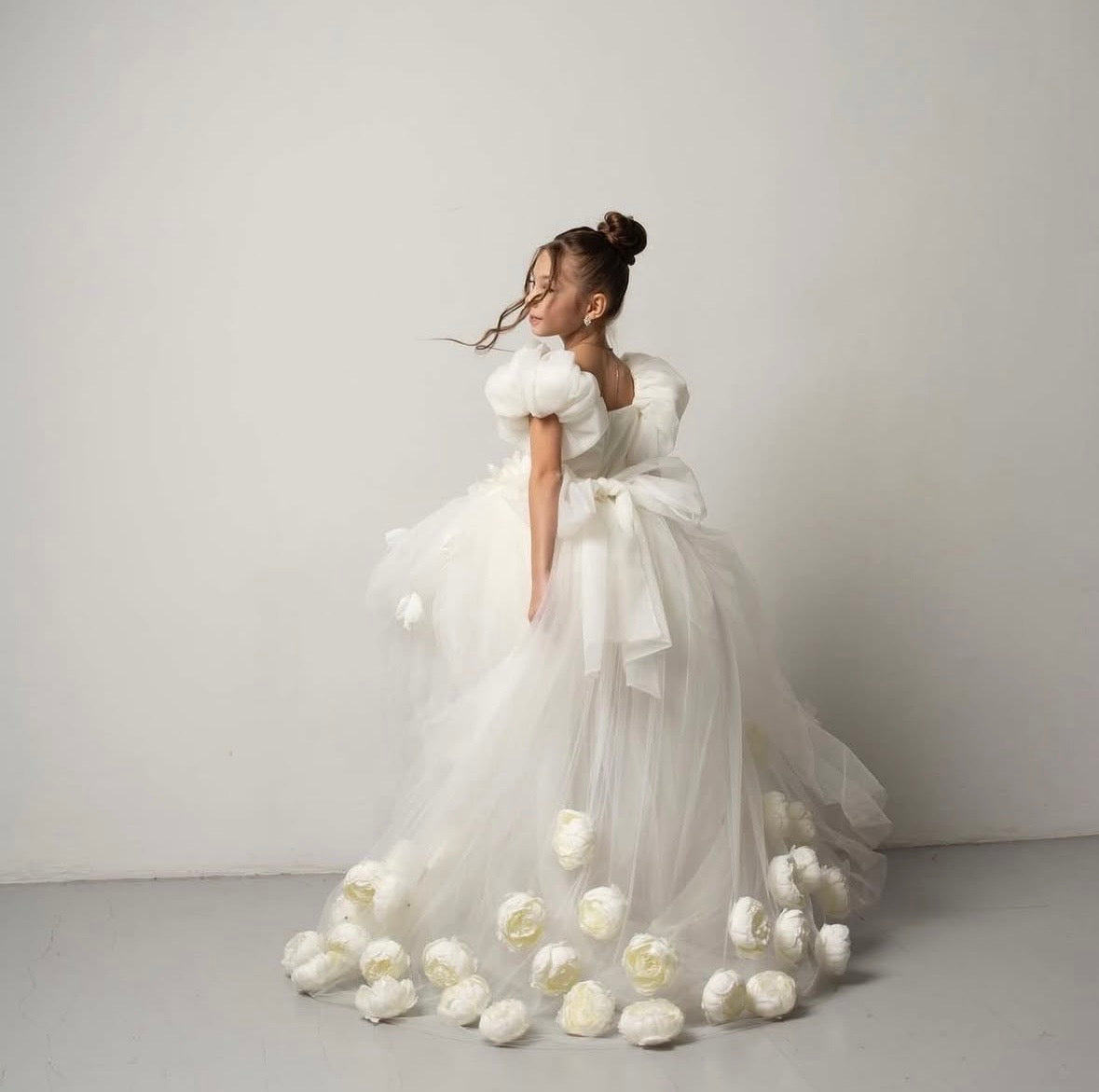     Robe de cérémonie enfant avec longue traîne ornée de fleurs séchées et manches bouffantes.